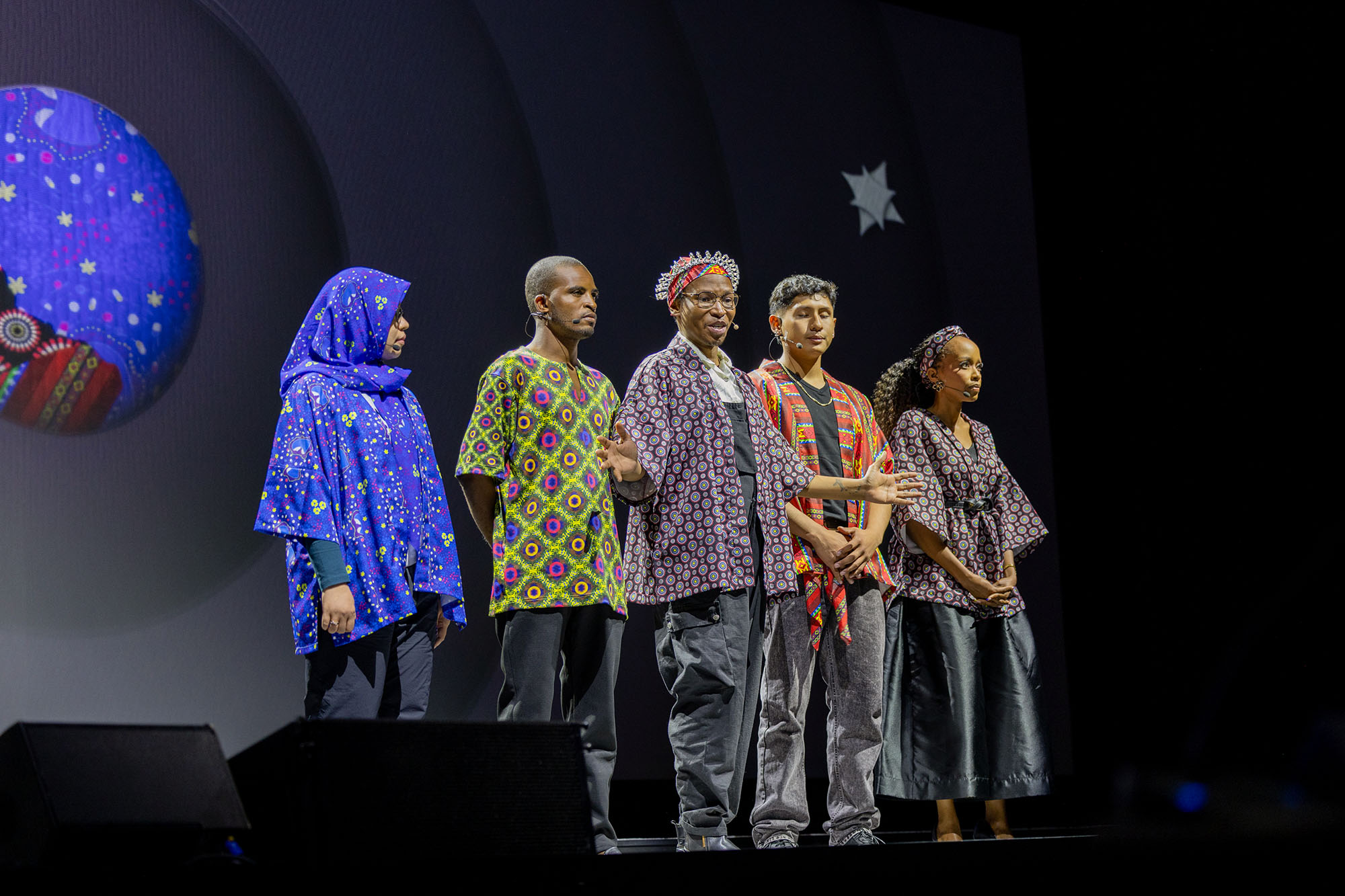 South African spoken word poet, writer and performer Xabiso Vili (center) is joined by global health advocates in an inspiring on-stage performance at the Global Fund’s Eighth Replenishment Summit in Johannesburg, South Africa, on 21 November 2025. The advocates’ stories are woven into the patterned fabrics they wear. Four fighters. Four journeys that speak to something far greater: our shared humanity and our vision of a better future. Each pattern tells a story of determination, purpose and the human spirit that rises again and again. From left to right on stage: Ani Herna Sari from Indonesia, Nuradeen Zakariyya from Nigeria, Xabiso Vili (center), Ivan Molina Aranibar from Bolivia and Sibulele Sibaca Nomnganga from South Africa.&nbsp;