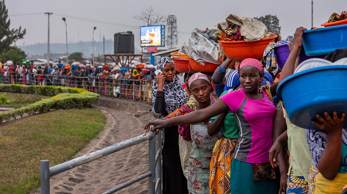 Des gens font la queue en attendant de passer la frontière entre Goma, en RDC, et Gisenyi, au Rwanda. Derrière eux, un écran diffuse des messages de sensibilisation à Ebola. Le Rwanda a mis en place un plan national détaillé de préparation à la lutte contre la maladie. (Nichole Sobecki / VII pour le Fonds mondial)